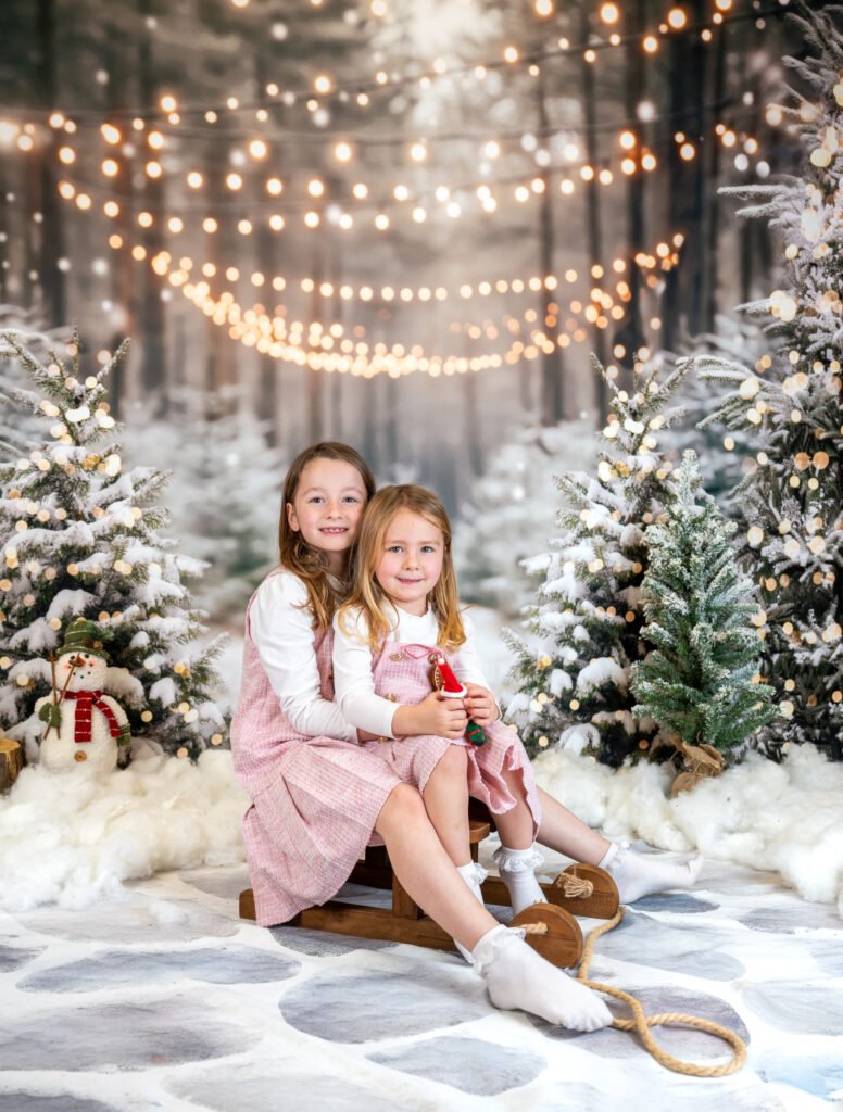 Two girls on a sled next to each other in a winter scene